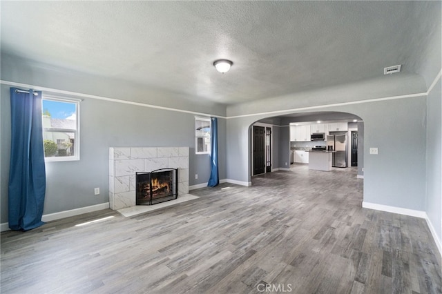 unfurnished living room featuring a tiled fireplace, baseboards, a textured ceiling, and wood finished floors