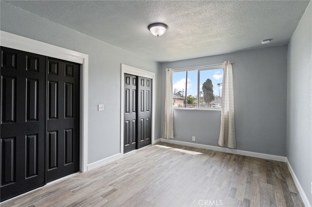 unfurnished bedroom with a textured ceiling, baseboards, and wood finished floors