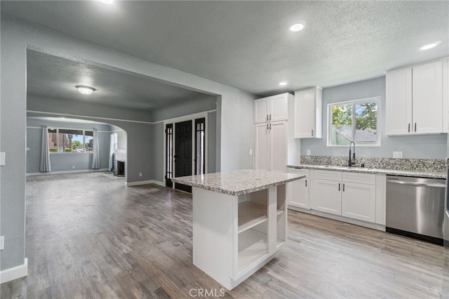 kitchen with stainless steel dishwasher, a sink, light wood-type flooring, a textured ceiling, and arched walkways