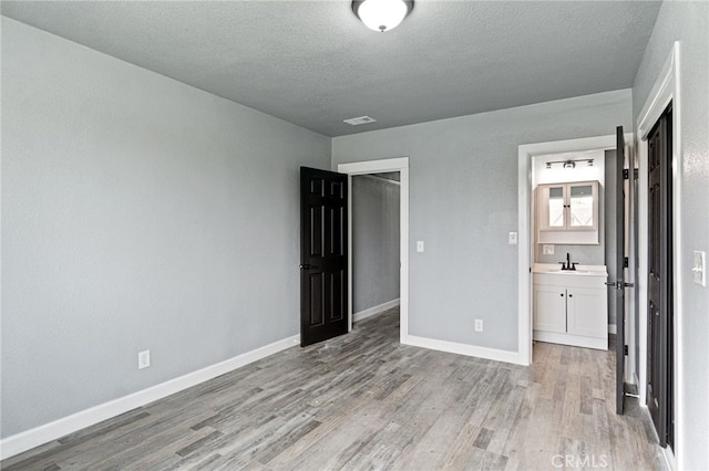 unfurnished bedroom with a textured ceiling, visible vents, a sink, baseboards, and light wood-style floors