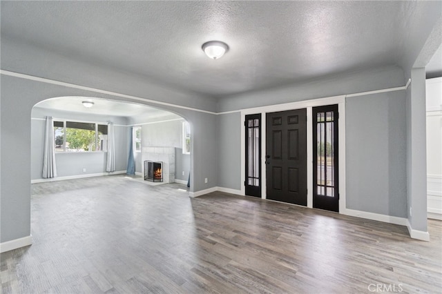 foyer entrance featuring a textured ceiling, a fireplace with flush hearth, arched walkways, wood finished floors, and baseboards