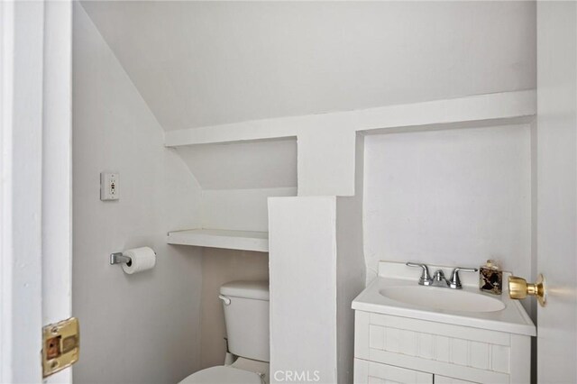 half bath featuring toilet, vaulted ceiling, and vanity