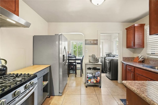 kitchen with light tile patterned flooring, light stone counters, stainless steel appliances, under cabinet range hood, and washer and clothes dryer