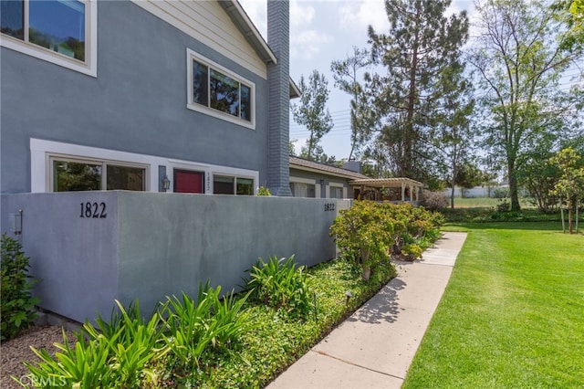 view of side of property featuring stucco siding, a yard, a chimney, and fence