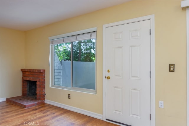 entryway featuring baseboards, a brick fireplace, and wood finished floors