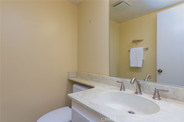 half bath with toilet, visible vents, and vanity
