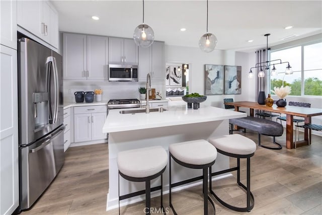 960 N Tangent Privado Unit 204, Ontario, CA 91764 - kitchen with a kitchen breakfast bar, appliances with stainless steel finishes, tasteful backsplash, light countertops, and light wood-style flooring