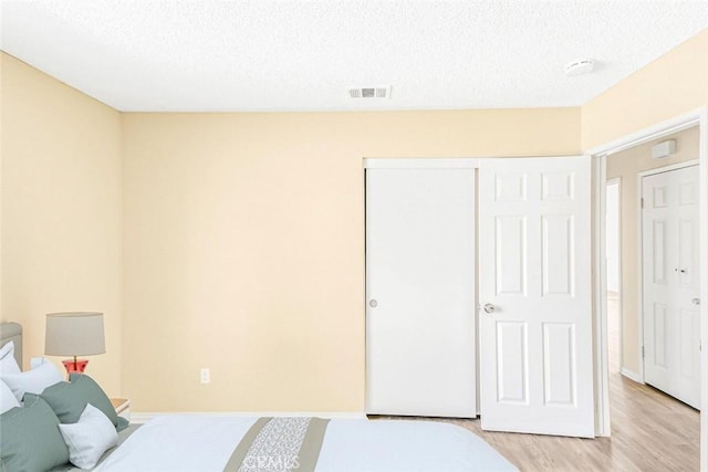 bedroom with a closet, a textured ceiling, visible vents, and light wood-type flooring