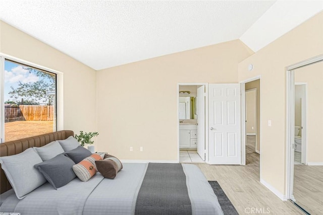 bedroom with ensuite bathroom, baseboards, a textured ceiling, light wood-style flooring, and vaulted ceiling