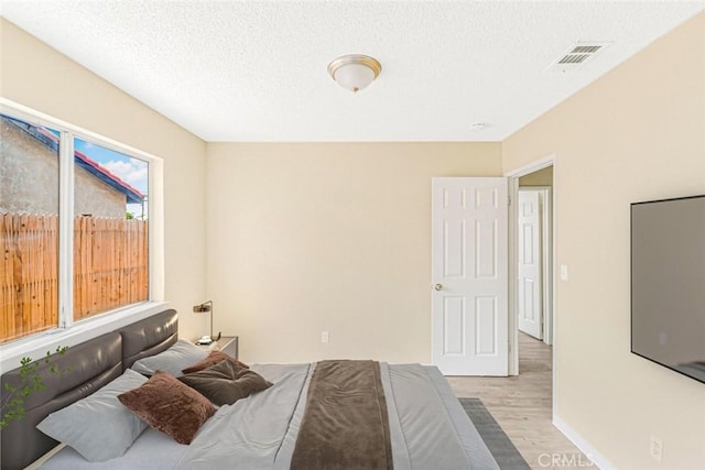 bedroom featuring baseboards, a textured ceiling, light wood-style flooring, and visible vents