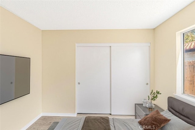 bedroom with a textured ceiling, baseboards, wood finished floors, and a closet
