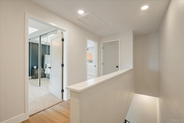 hall with recessed lighting, attic access, light wood finished floors, and an upstairs landing
