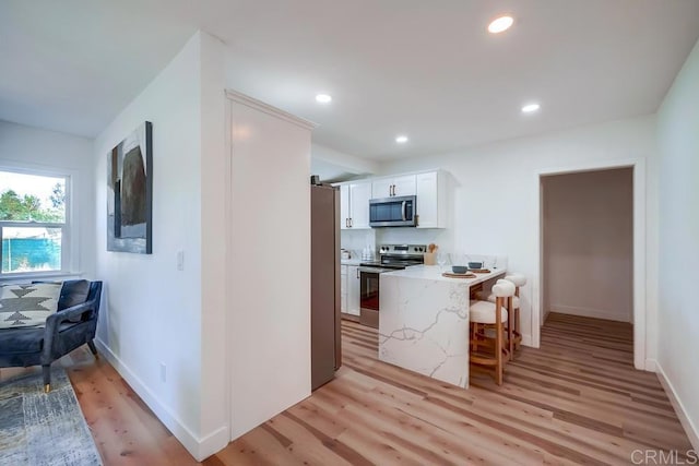 kitchen with a kitchen bar, light stone counters, white cabinets, stainless steel appliances, and light wood-style flooring