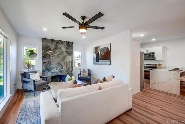 living room with recessed lighting, a ceiling fan, light wood finished floors, and a high end fireplace