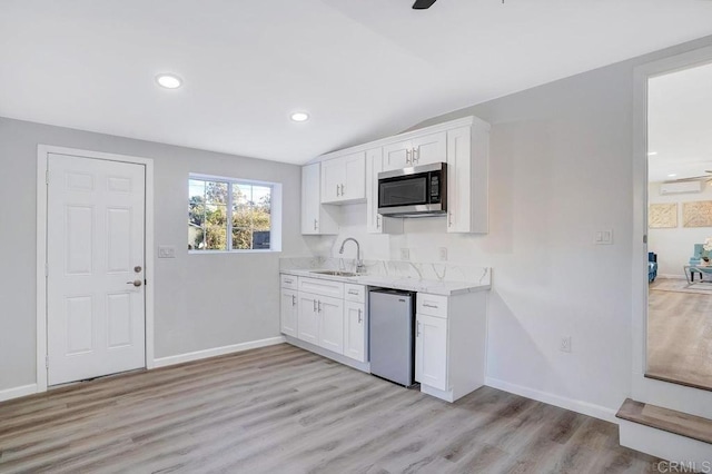 kitchen with lofted ceiling, light wood-style floors, white cabinets, a sink, and stainless steel appliances