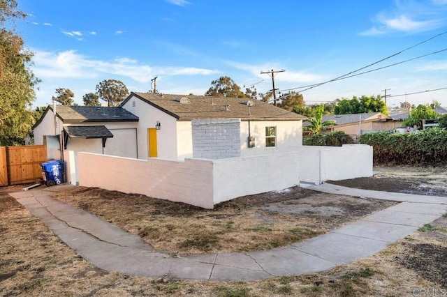 view of front of property featuring fence, a shingled roof, and stucco siding