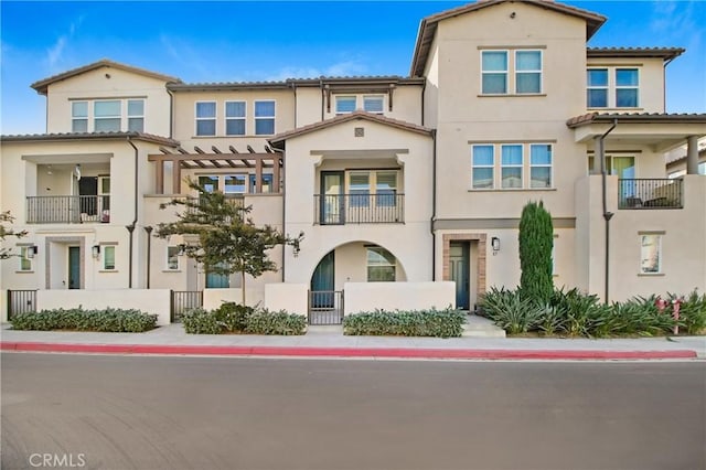 townhome / multi-family property with a fenced front yard, a tile roof, stucco siding, a gate, and a balcony