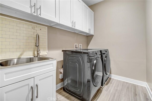 laundry room featuring independent washer and dryer, cabinet space, a sink, baseboards, and light wood-style flooring