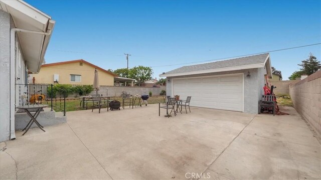 view of patio / terrace with a detached garage, an outdoor structure, a fenced backyard, and an outdoor fire pit