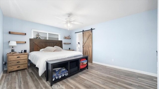 bedroom with baseboards, a barn door, ceiling fan, and wood finished floors