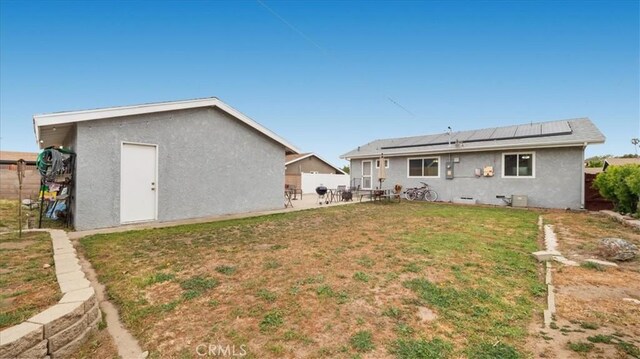 rear view of property with fence, stucco siding, a patio area, a lawn, and solar panels