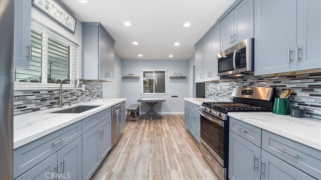 kitchen with a sink, appliances with stainless steel finishes, light wood-style floors, and a wealth of natural light