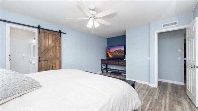 bedroom with ceiling fan, a barn door, light wood finished floors, baseboards, and visible vents