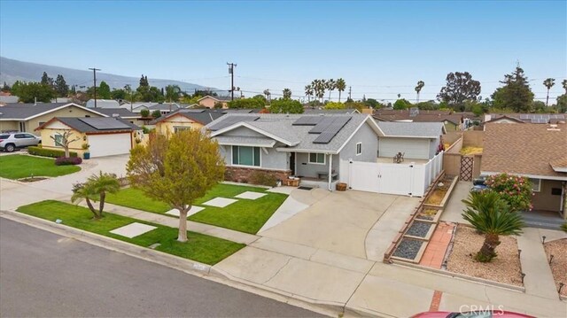 single story home with a residential view, a front yard, a gate, solar panels, and driveway