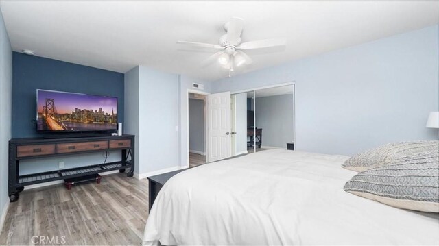 bedroom featuring ceiling fan, visible vents, wood finished floors, baseboards, and a closet