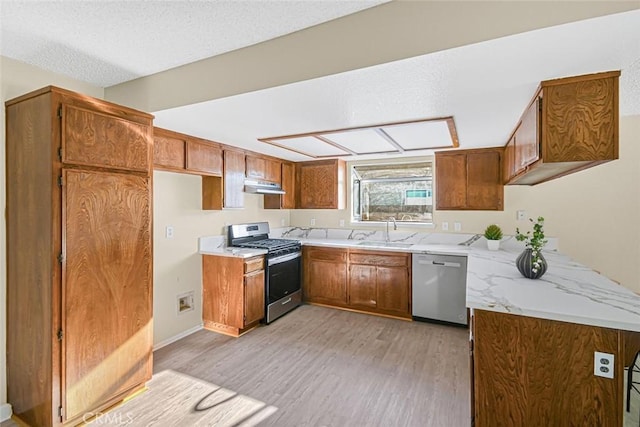 kitchen featuring brown cabinets, appliances with stainless steel finishes, a sink, light wood-type flooring, and under cabinet range hood