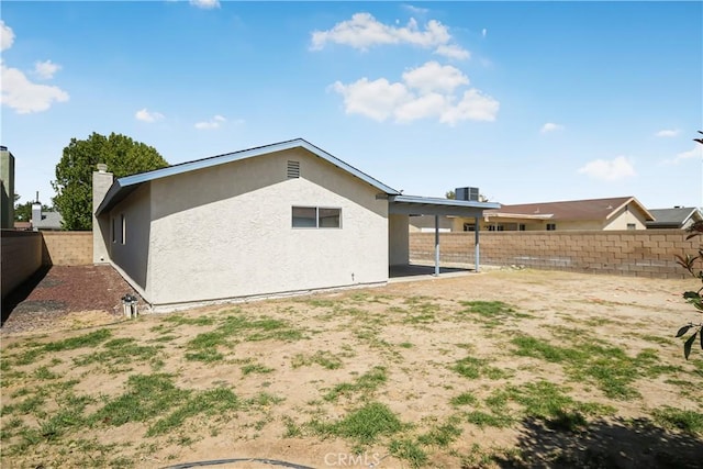 rear view of house featuring a fenced backyard, stucco siding, a chimney, and central AC unit