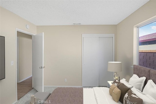 bedroom featuring a textured ceiling, visible vents, baseboards, and a closet