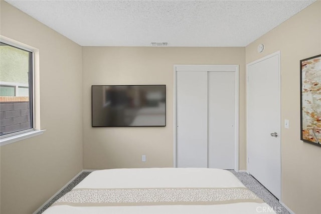 carpeted bedroom featuring visible vents, a textured ceiling, baseboards, and a closet