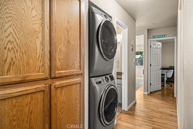 laundry room with light wood-style floors, baseboards, laundry area, and stacked washer and dryer