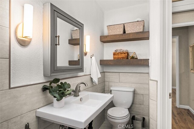 half bathroom with toilet, a sink, wood finished floors, and tile walls