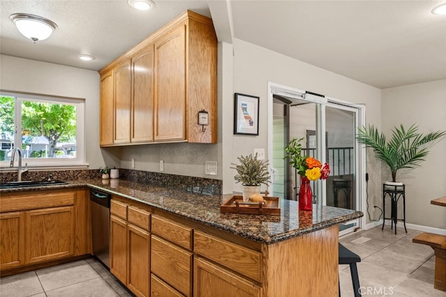 kitchen featuring a breakfast bar area, dishwasher, a sink, dark stone counters, and light tile patterned flooring