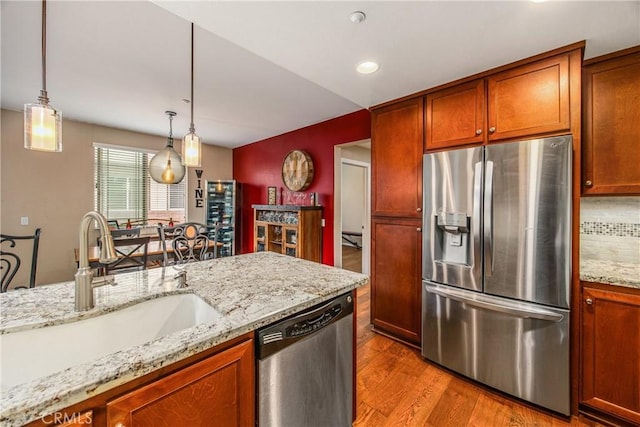 kitchen with decorative light fixtures, wood finished floors, a sink, light stone counters, and stainless steel appliances