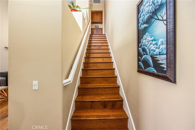 staircase featuring baseboards, wood finished floors, and visible vents