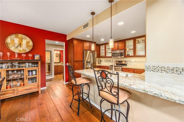 kitchen featuring visible vents, light stone countertops, a peninsula, a breakfast bar, and stainless steel appliances