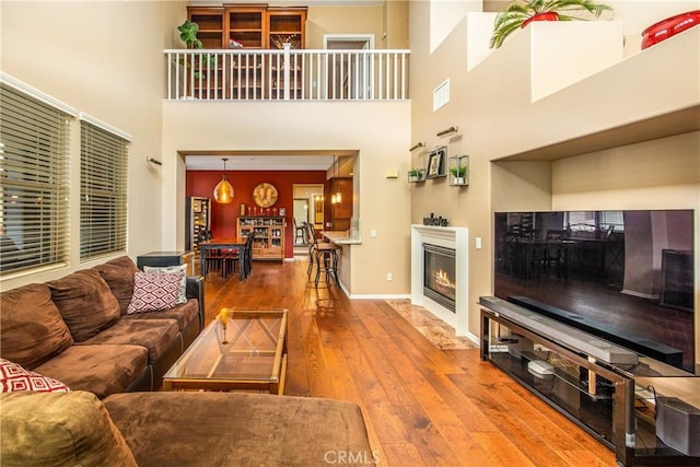 living area featuring visible vents, a towering ceiling, baseboards, wood-type flooring, and a glass covered fireplace