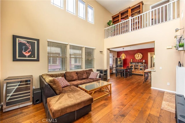 living room featuring baseboards, a high ceiling, wood-type flooring, and beverage cooler