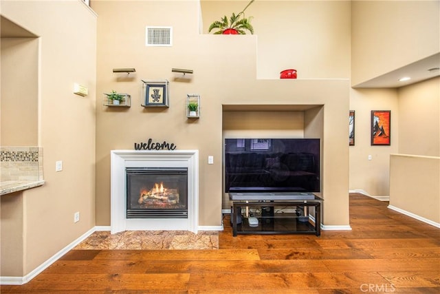 living room featuring a glass covered fireplace, baseboards, wood finished floors, and visible vents