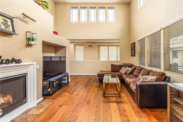 living room featuring a glass covered fireplace, baseboards, wood-type flooring, and a towering ceiling
