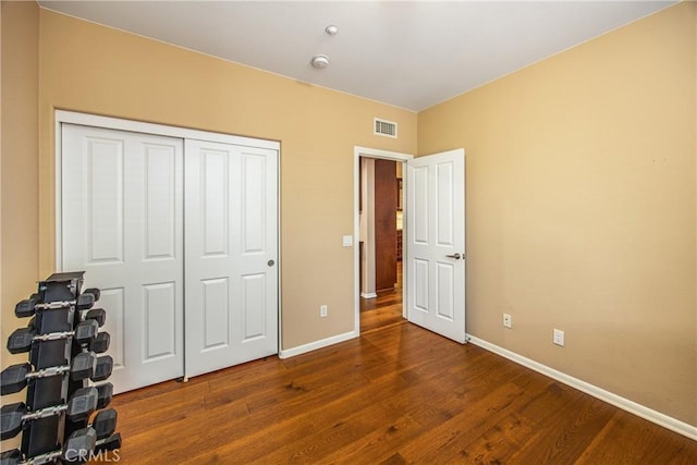 bedroom with baseboards, visible vents, wood finished floors, and a closet