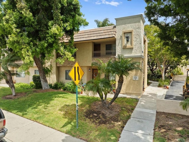 view of front of property with a tile roof, a balcony, a front yard, and stucco siding