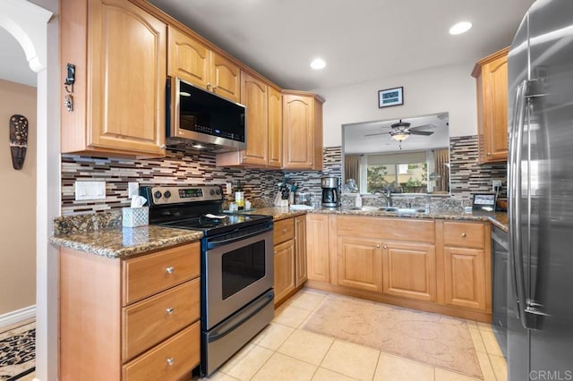 kitchen with ceiling fan, backsplash, appliances with stainless steel finishes, a sink, and dark stone countertops