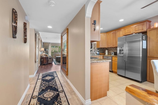 kitchen with decorative backsplash, light stone countertops, recessed lighting, arched walkways, and stainless steel appliances
