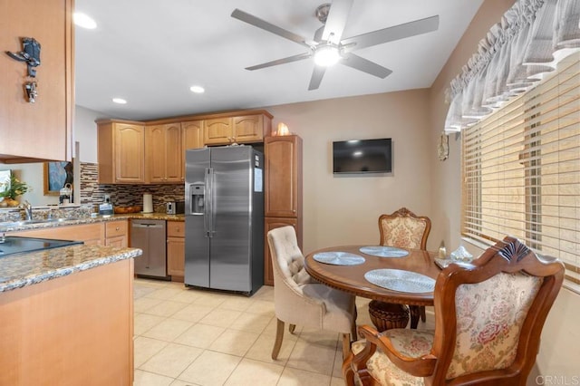 kitchen with decorative backsplash, ceiling fan, a sink, stone countertops, and stainless steel appliances