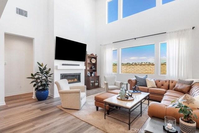 living room with a towering ceiling, plenty of natural light, light wood-type flooring, and visible vents