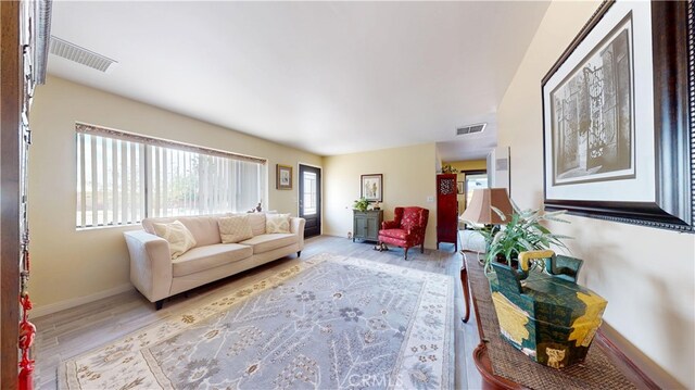 living room with visible vents, light wood-style flooring, and baseboards